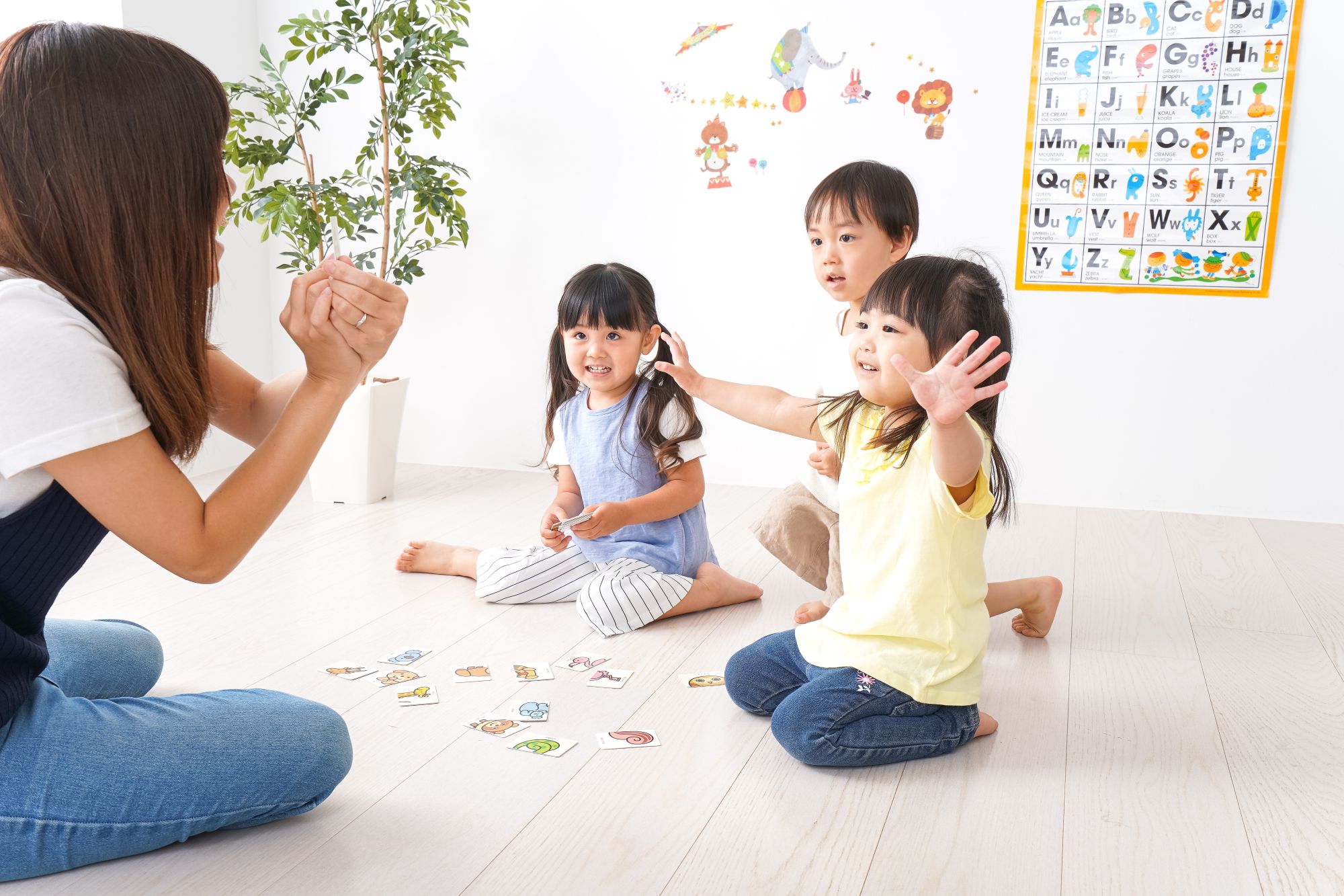 3 children seated on the floor happily enagaged by a teacher who is showing them a picture card