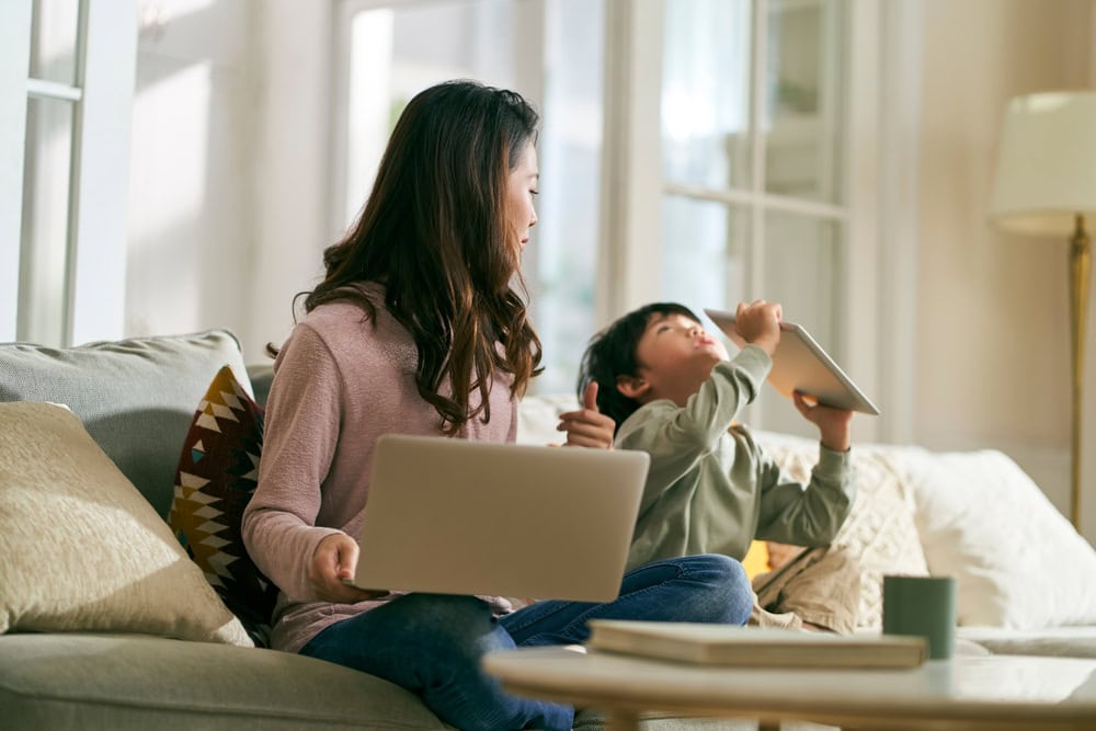 Positive, Not Permissive: Redefining discipline for today’s parents 5 A mother sitting on the sofa working on her laptop, with her is her child who is distracted from his tablet