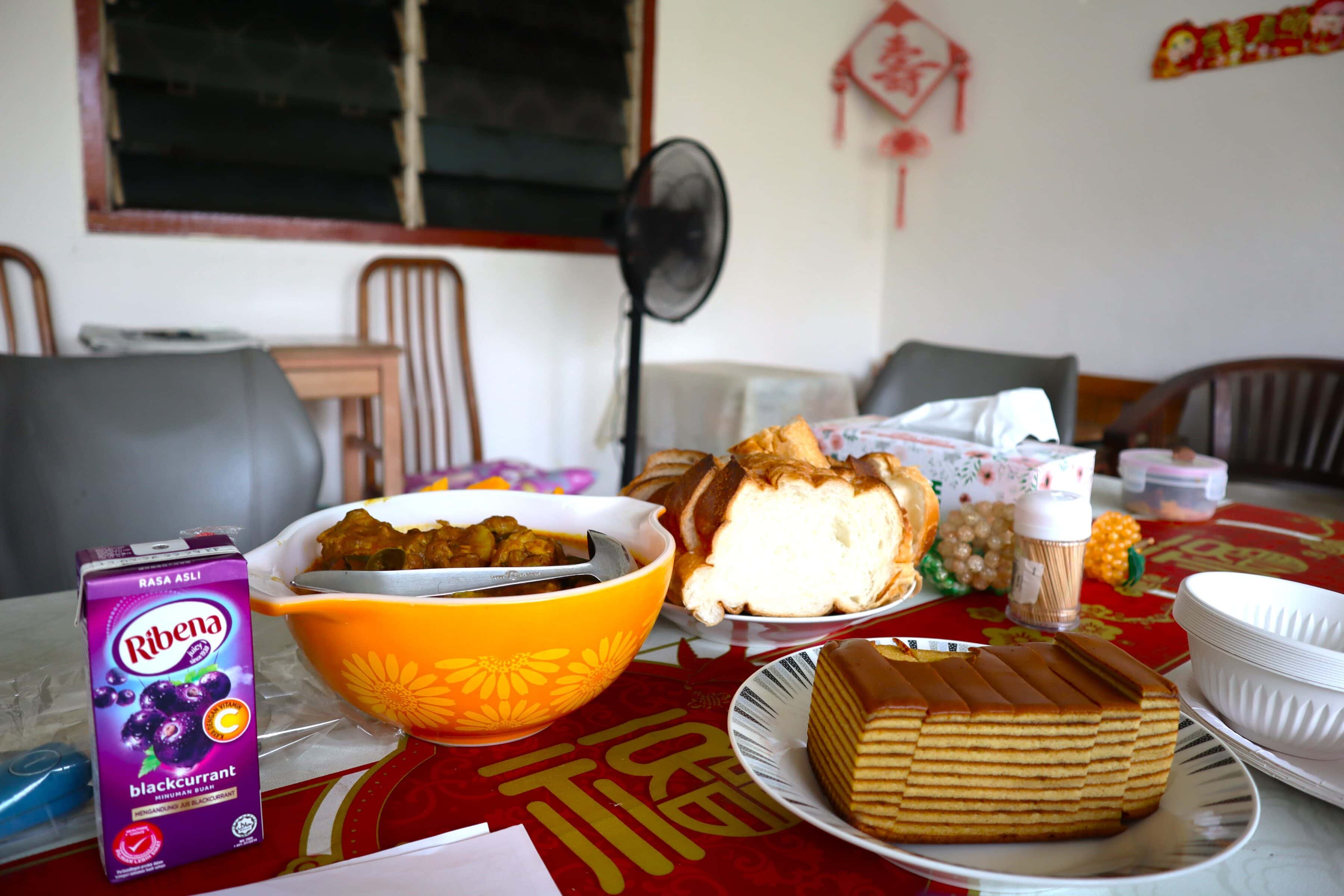 On the table is food Auntie Molly's helper prepared, including a juice box, a wbole of curry chicken, sliced french loaf and sliced kueh lapis