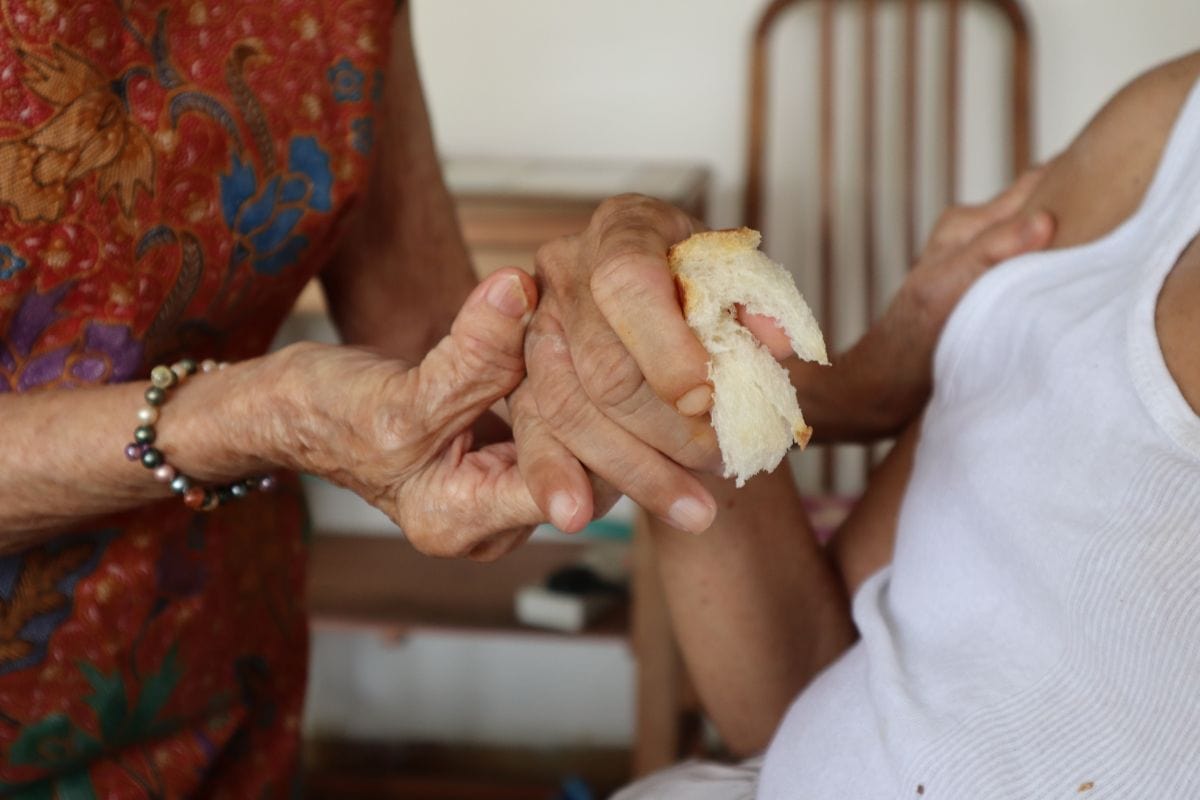 Auntie Molly's hands cupping her youngest son Mr Lee's as he holds onto a piece of bread.
