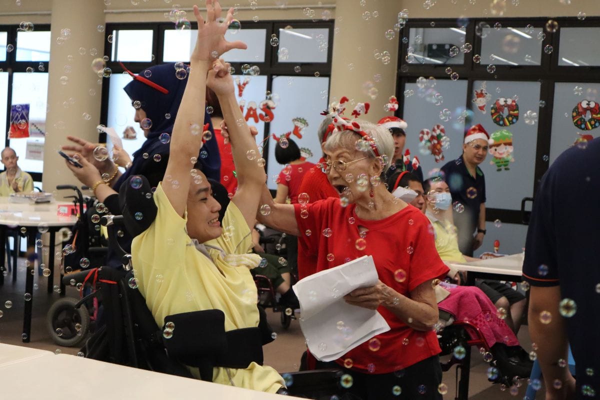 Auntie Molly singing enthusiastically with a D A C client who is in a wheelchair. Bubbles are in the fore- and background.