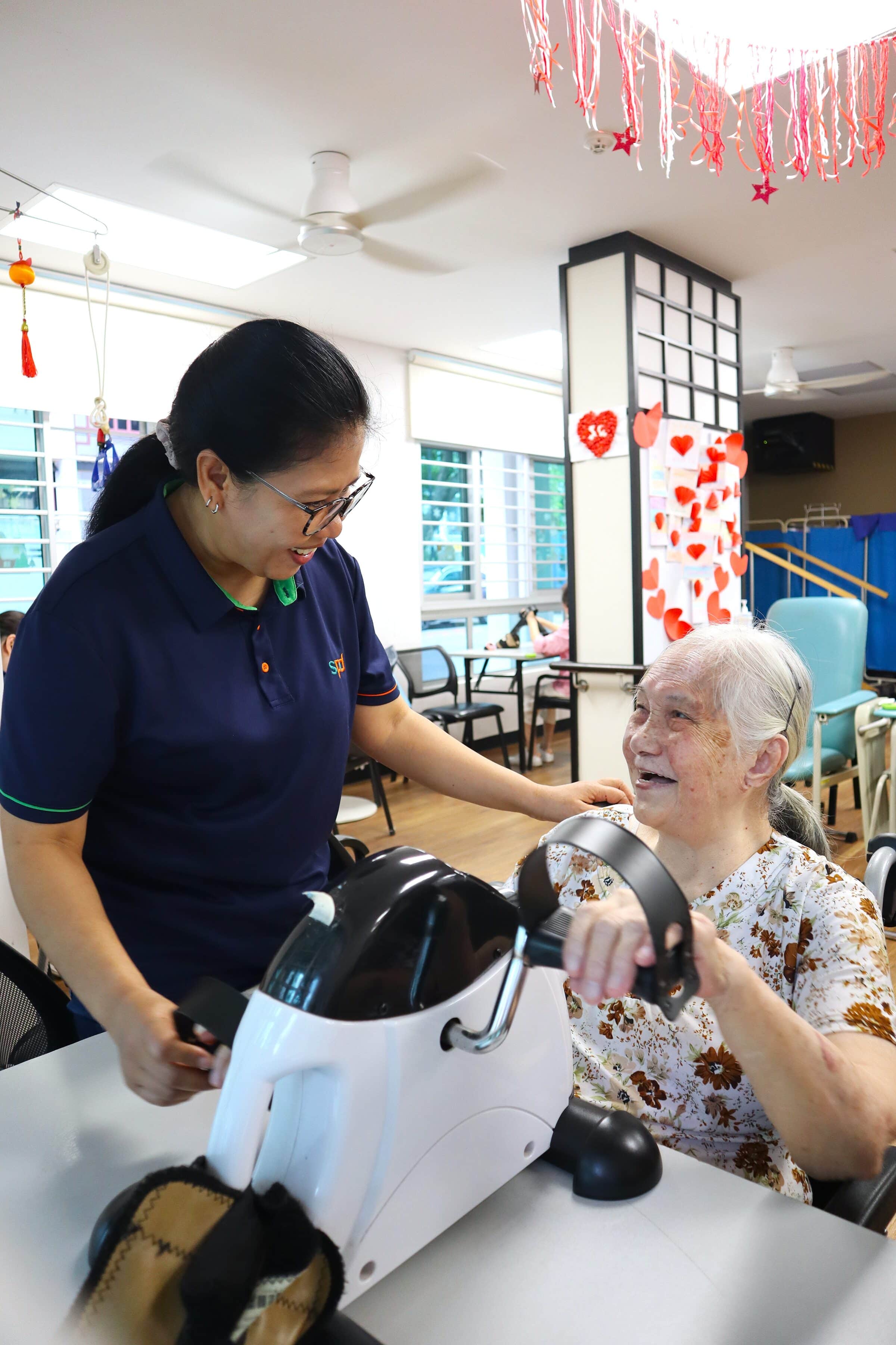 Mas Ayu guiding a senior client who is on the hand-cycle