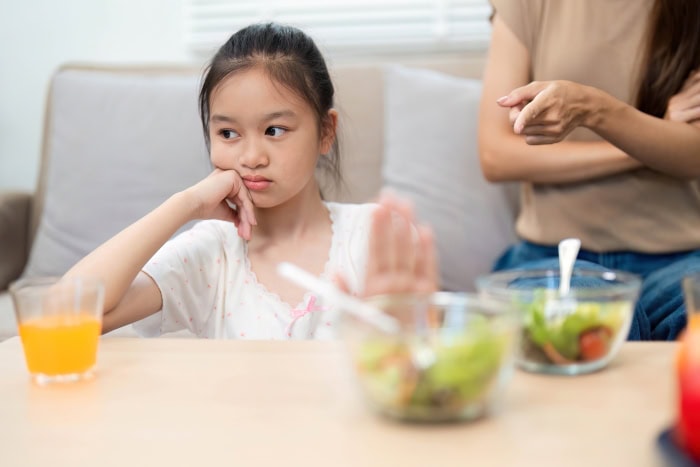 A child looks away and pushes away a bowl of vegetables