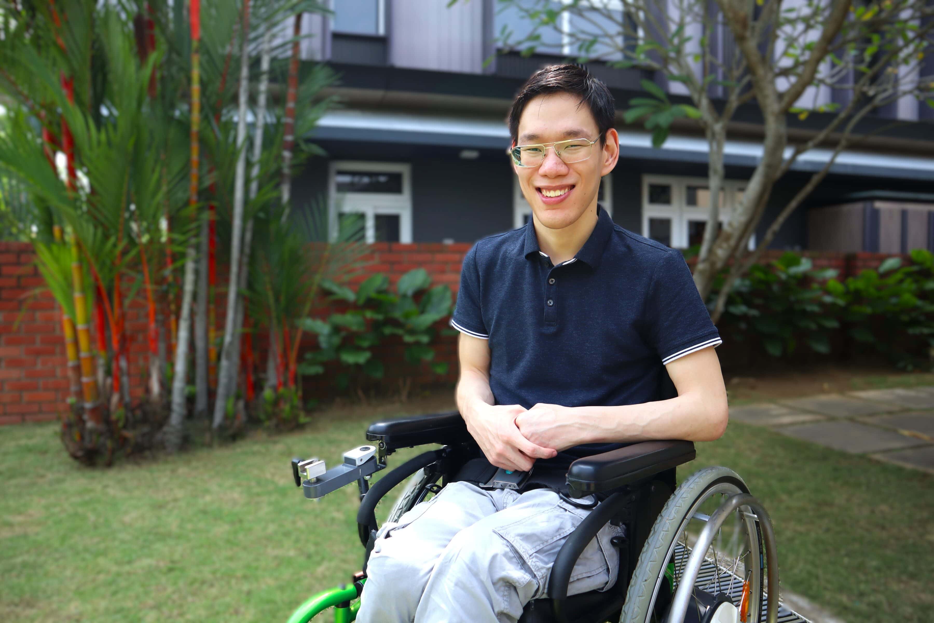 Zachary in a garden, seated in his wheelchair and smiling