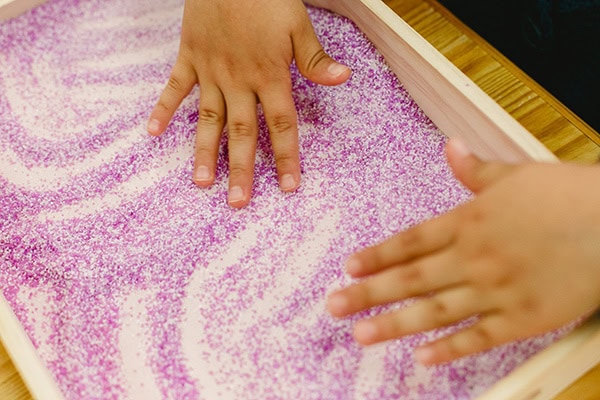 Fun activities to build early literacy at home 4 Little hands playing on a purple salt tray