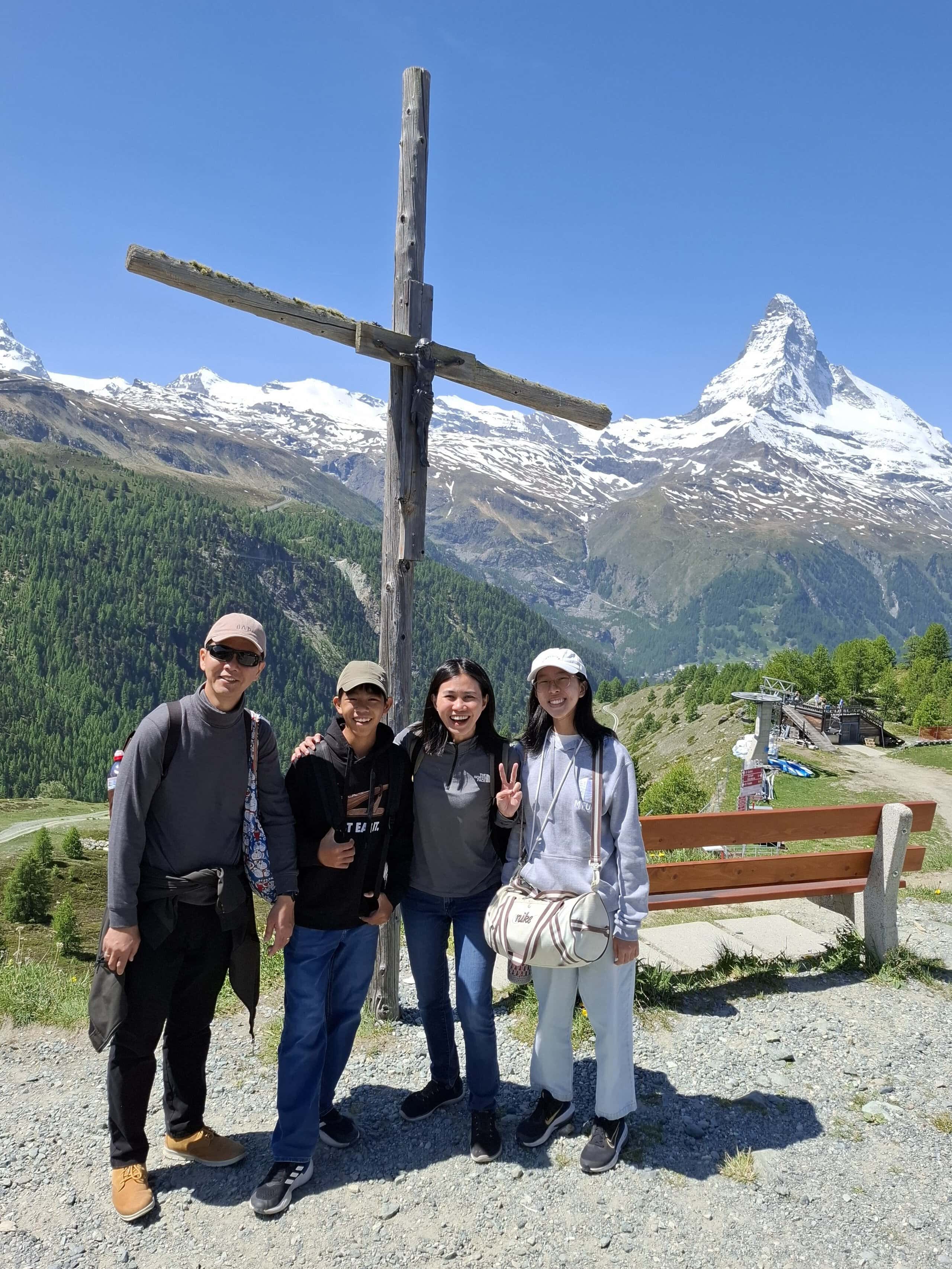 A Working Mum’s Perspective on Excellence - Lessons from Dr May Lim 3 Dr May Lim with her family overseas, behind her is a wooden cross and in the background is a snow-covered mountain
