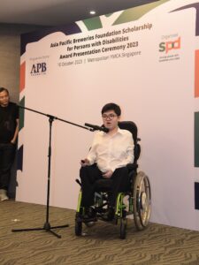Aaron speaking at A P B Scholarship for Persons with Disabilities Award Presentation Ceremony on 10 October 2023. His father, Mr Sim on the left hand corner of the photo looking at Aaron proudly.
