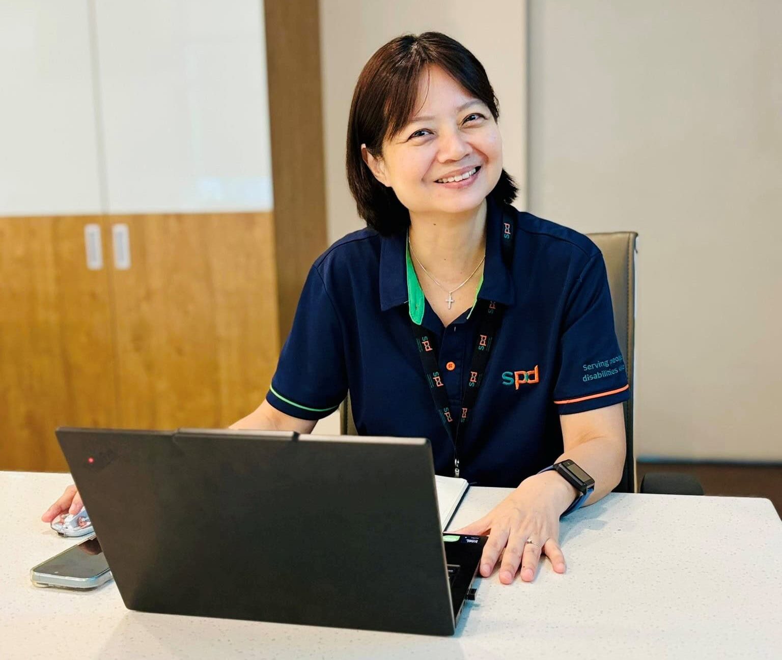 Sharon smiling in the camera seated in a meeting room with laptop in front of her